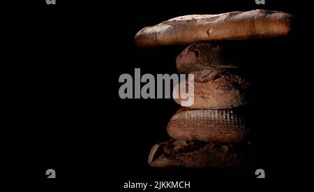 Bunch of delicious freshly baked bread loaves and baguette stacked on top of each other against black background in studio Stock Photo