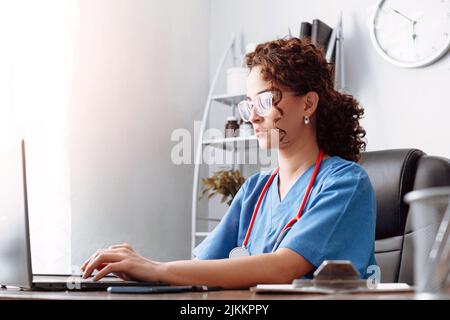 Young hispanic woman wearing health uniform using a laptop. Stock Photo
