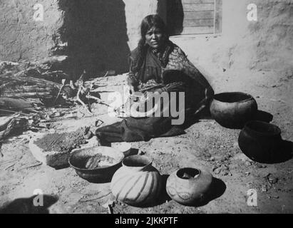 Black and white historical photograph of a Pueblo woman making and selling large traditional pots Stock Photo