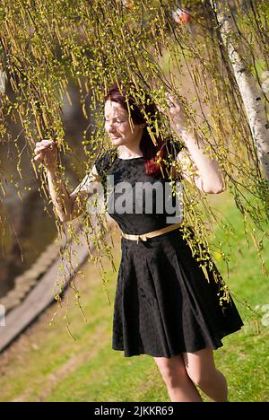 A vertical shot of a beautiful Caucasian woman enjoying the sunny weather surrounded by greenery Stock Photo