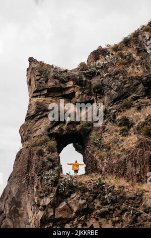 A vertical shot of  man in a yellow jacket enjoys nature standing on a rock Stock Photo