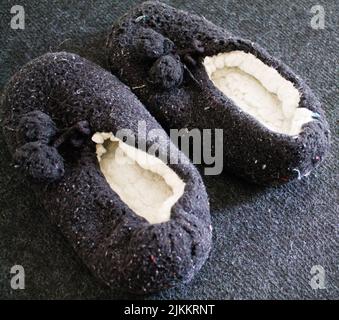 A closeup of a pair of used black fluffy slippers on a rug at home Stock Photo