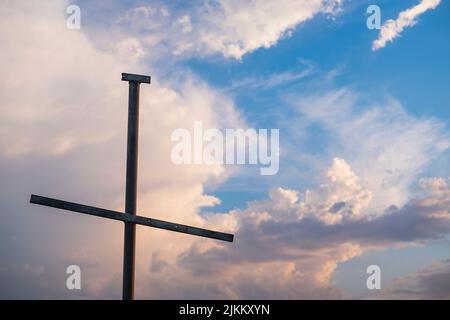 A closeup of a metallic cross against a beautiful blue cloudy sky Stock Photo