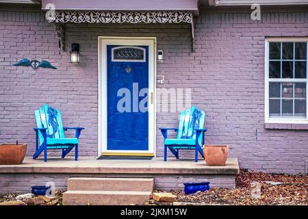 Blue mermaid adirondack chairs sit on porch of brick house painted purple with blue front door Stock Photo