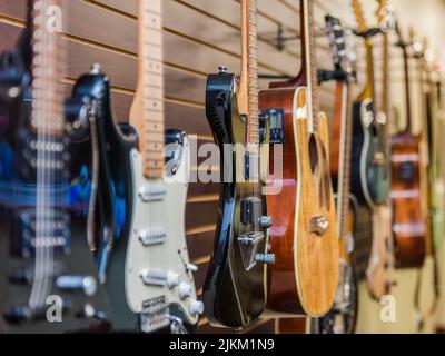 A closeup shot of the various types of guitars hanging on the wall in the music store Stock Photo