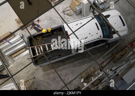 Caucasian Contractor Worker in His 30s and His White Modern Pickup Truck on a Construction Site. Ceiling Top View. Construction Industry Theme. Stock Photo