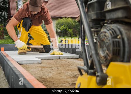 Residential Pathway Concrete Bricks Paving by Caucasian Worker. Compacting Machine in a Front. Stock Photo
