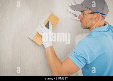 Caucasian Worker in His 40s Softly Applied Modern Vinyl Wallpaper Using Squeegee. Home Improvement Theme. Stock Photo