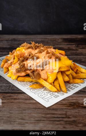 A closeup shot of a cheesy French fries on a paper on wooden table Stock Photo