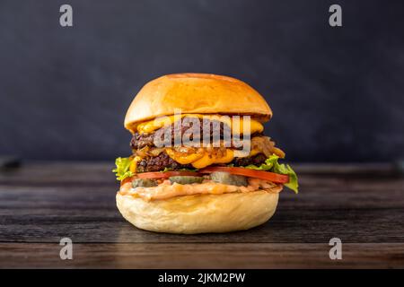 A closeup shot of a bacon burger sandwich with fries, lettuce, melted cheese, sweet onions and tomato double patty on wooden table Stock Photo