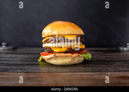 A closeup shot of a bacon burger sandwich with fries, lettuce, melted cheese, sweet onions and tomato double patty on wooden table Stock Photo
