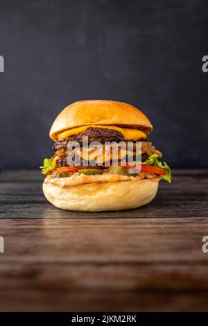 A vertical shot of a burger with bacon, fries, lettuce, melted cheese, crispy sweet onions and tomato Stock Photo