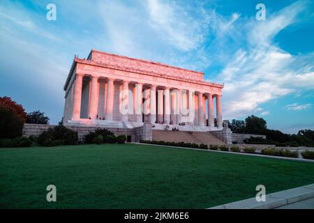 Pink light from sunrise illuminates the east-facing columns and exterior of the Lincoln Memorial in Washington, DC. Several sightseers sit on the step. Stock Photo