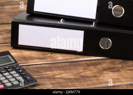 A closeup shot of black file folders with a calculator on a wooden background Stock Photo