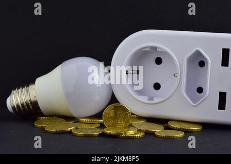 A closeup shot of electric multi plug adapter, led lamp, and coins on a gray background Stock Photo