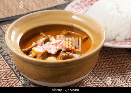 A closeup shot of a Chicken Thai red curry and a white rice plate on a decorated table Stock Photo