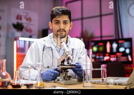 Modern medical research laboratory: portrait of scientist working, using microscope, analyzing samples. Advanced scientific pharmaceutical lab for medicine, biotechnology development. Stock Photo
