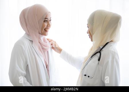 Two young Thai Muslim women doctors talking together against a white background Stock Photo