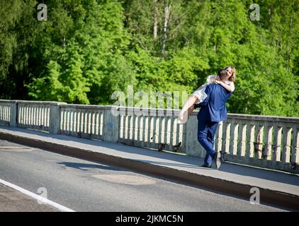 A view of the beautiful couple- the groom carrying the bride in his arms and trees in the background Stock Photo