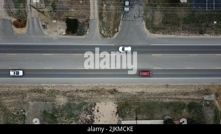 An aerial top view of cars driving on the asphalt road surrounded by green lawn Stock Photo