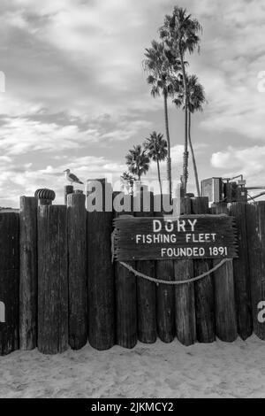 A grayscale shot of the Dory Fishing Fleet sign on a wooden fence in Newport Beach California, USA Stock Photo