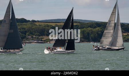 Cowes, Isle of Wight, England, UK.2022. Racing yachts sailing  past the the Isle of Wight coastline during Cowes Week regatta Stock Photo