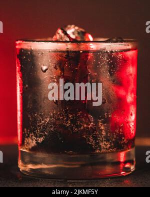 A vertical closeup of a soda drink with ice cubes in it against a red neon background Stock Photo