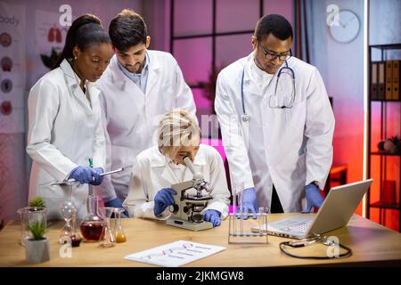 Modern medical research laboratory: portrait of group young scientists using microscope, digital laptop, doing sample analysis, talking. Diverse team of multi-ethnic specialists work in advanced lab Stock Photo