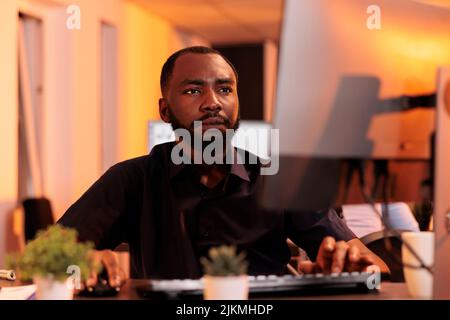 Confident businessman analyzing data charts on computer, doing research to create project report online on company network. Working with web information and sending email with documents. Stock Photo