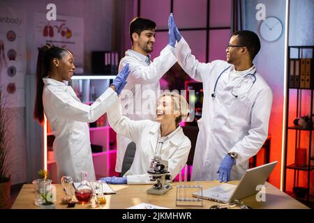 Professional international medical scientists giving high five after ending of the experiment in modern biology laboratory. Stock Photo