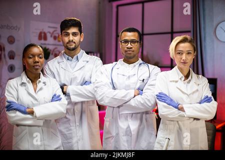 Smiling group of scientists in modern laboratory with male african american leader, mix race team of scientific researchers in lab wearing white coats and stethoscopes Stock Photo