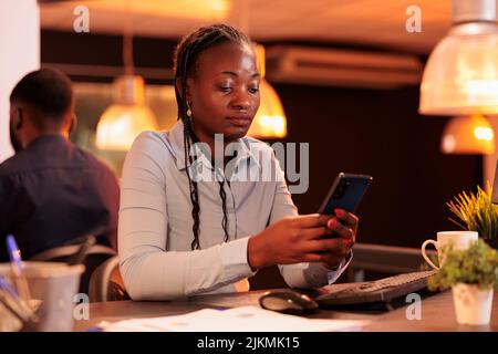 Office worker looking at smartphone app to plan presentation, using social media website to create email report. Analyzing online data on mobile phone to do paperwork research. Stock Photo