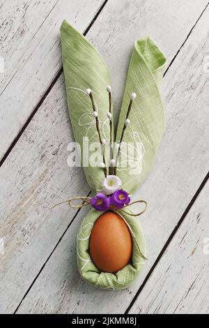 Decorative Bunny Ears from green napkin with egg on natural wooden background to Celebrate Easter, DIY, flat lay Stock Photo