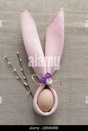 Decorative Bunny Ears from napkin with egg on natural cotton tablecloth to Celebrate Easter, DIY, flat lay Stock Photo