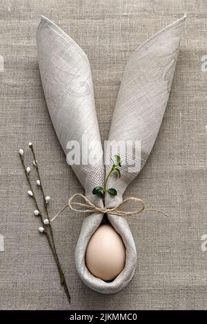 Decorative Bunny Ears from napkin with egg on natural cotton tablecloth to Celebrate Easter, DIY, flat lay Stock Photo