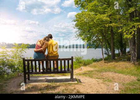 Young loving couple cuddled together on a bench in a lake in summer. Stock Photo