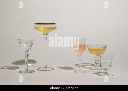 arrangement of different cocktail glasses on white background with pink and gold liquid Stock Photo