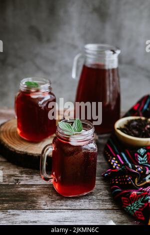 Agua de Jamaica or roselle mocktail drink, summer beverage in mexico with ice and dry hibiscus petals on table background Stock Photo