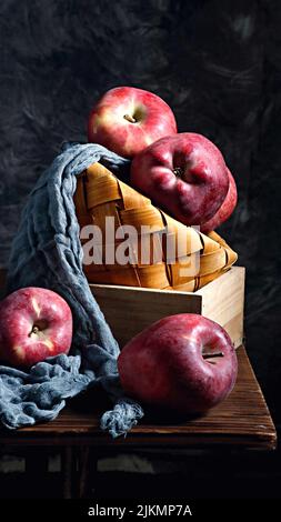 A straw basket with red apples on a wooden table with a dark background Stock Photo