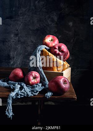 A Straw basket with red apples on a wooden table with a dark background Stock Photo