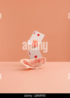 A slice of grapefruit and playing heart cards on a light pink background Stock Photo