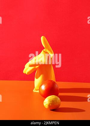 A closeup shot of fresh ripe Lemon, tomato and single heavy duty yellow rubber glove on an orange table against red wall Stock Photo