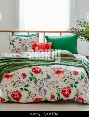 A beautiful shot of a bed with pillows and flowery sheet with white curtains on the window Stock Photo