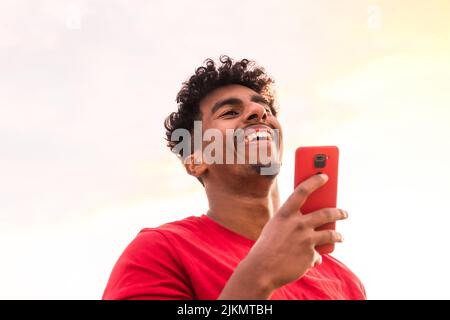 Arab young man with red t-shirt in a sunset sending a voice note with the mobile in the city Stock Photo