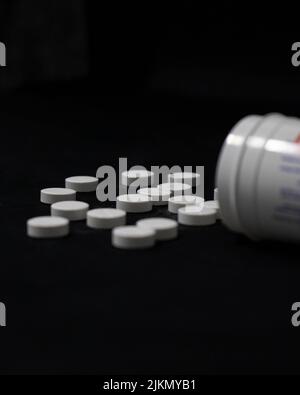 A closeup shot of a pile of medical pills with an open bottle on a dark background Stock Photo