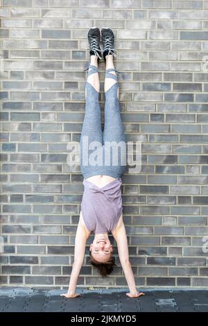 young woman makes a handstand in front of a stone wall as a fitness workout Stock Photo