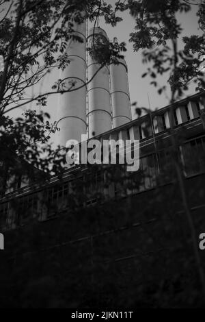 A vertical low angle grayscale shot of the industrial factory in the distance Stock Photo