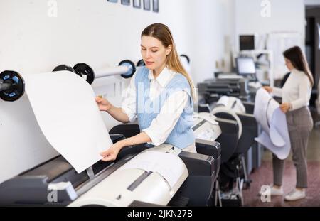 Print worker controlling printing process on modern offset machine in print shop Stock Photo