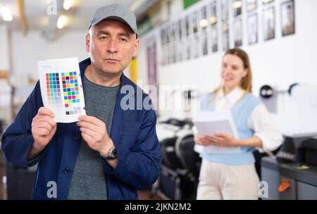 Service engineer demonstrating test page with color palette in his hand ...