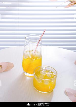A vertical shot of an aesthetic composition with orange juice in glass cups with ice cubes on a table Stock Photo